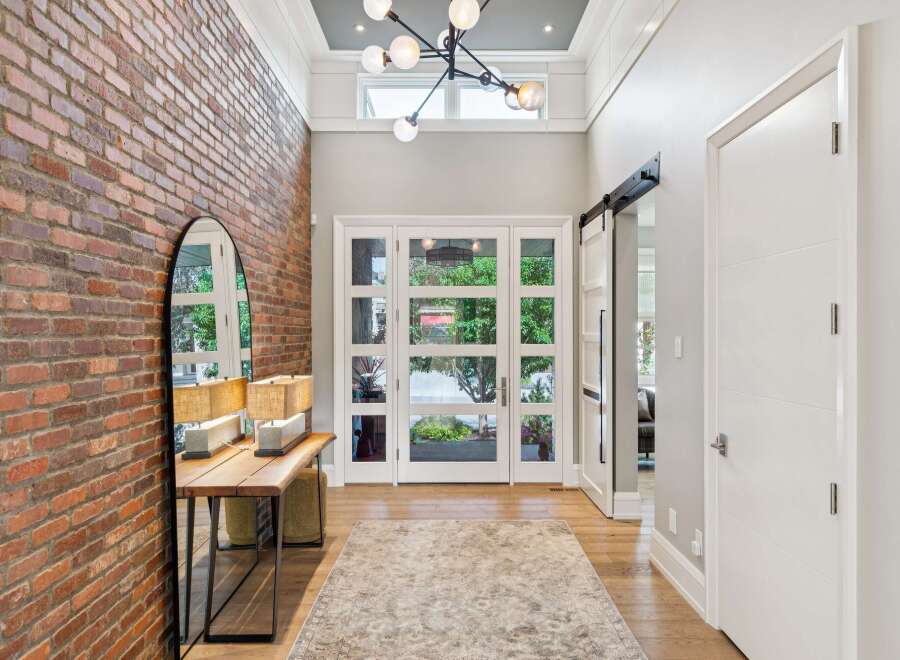 Step into a grand foyer featuring a striking exposed brick accent wall and a modern chandelier.