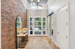 Step into a grand foyer featuring a striking exposed brick accent wall and a modern chandelier.