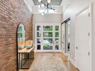 Step into a grand foyer featuring a striking exposed brick accent wall and a modern chandelier.