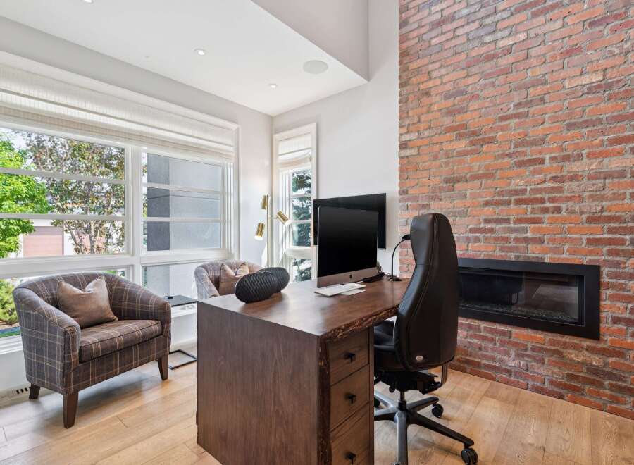 This home office features a rustic live-edge desk paired with a comfortable black leather office chair, set against a striking exposed brick wall with a modern fireplace.
