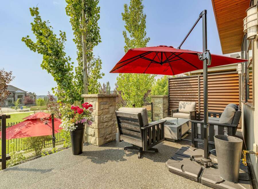 Enjoy outdoor living with this stunning patio featuring comfortable seating, a modern fire pit, and a vibrant red umbrella for shade.