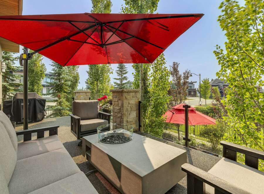 Enjoy outdoor living with this spacious patio featuring comfortable seating, a modern fire pit table, and a large red umbrella for shade.
