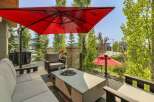 Enjoy outdoor living with this spacious patio featuring comfortable seating, a modern fire pit table, and a large red umbrella for shade.