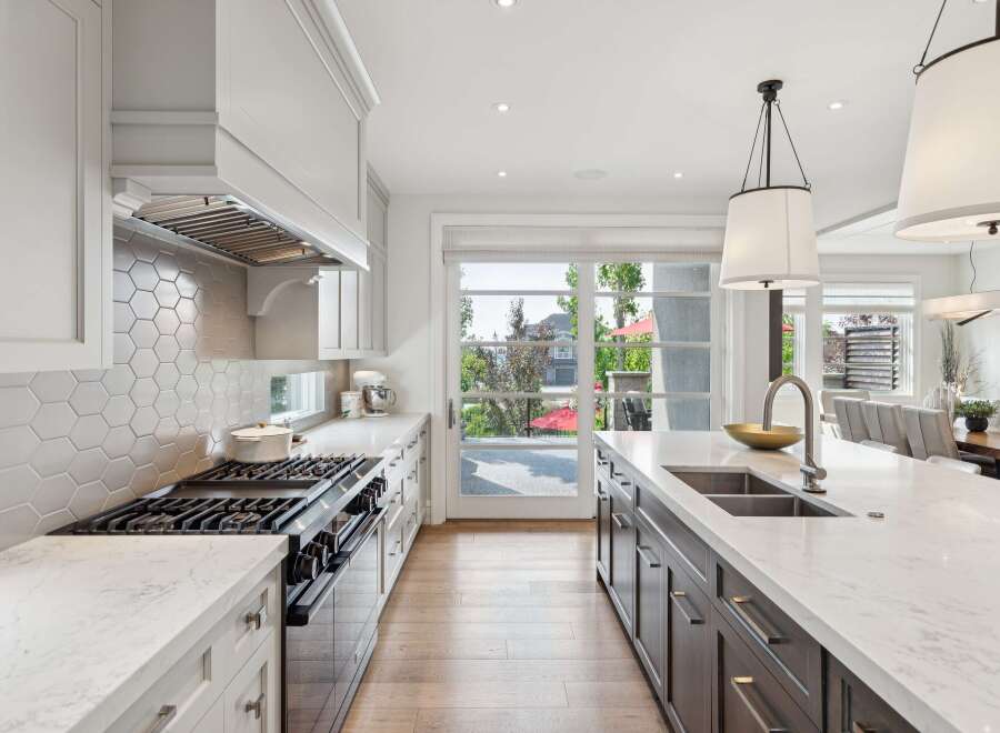 Experience luxury in this stunning modern kitchen, featuring a sleek gas range with a hexagonal tile backsplash and a spacious island with a double sink.