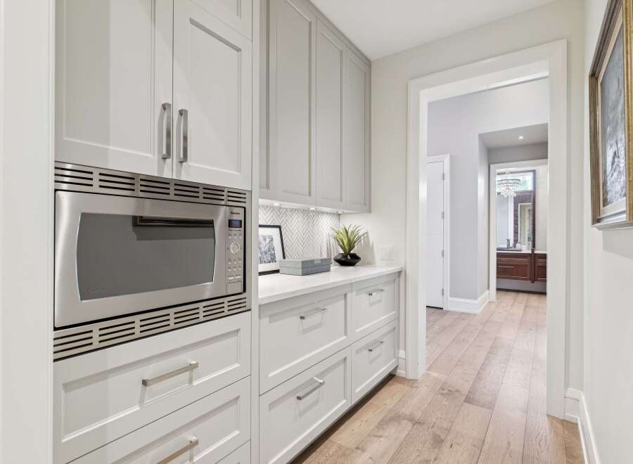 Discover this beautifully appointed kitchen pantry, featuring sleek grey cabinetry and a modern stainless steel microwave.