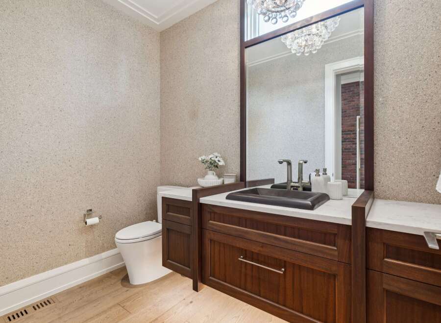This elegant powder room features a textured wallpaper, a dark wood vanity with a marble countertop, and a modern vessel sink.