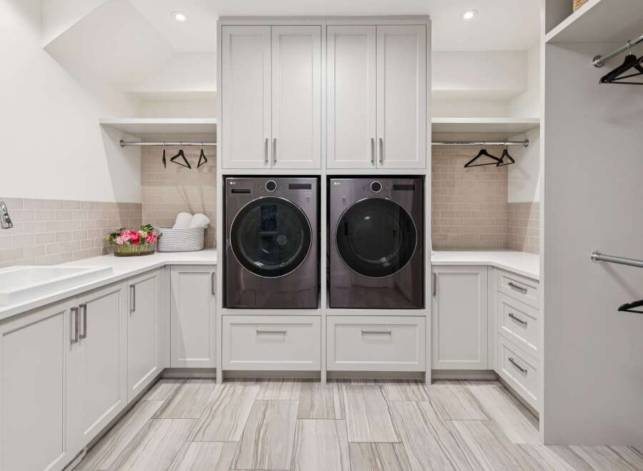 This modern laundry room features a sleek design with stacked LG washers and dryers, ample cabinet storage, and a large sink.