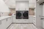 This modern laundry room features a sleek design with stacked LG washers and dryers, ample cabinet storage, and a large sink.