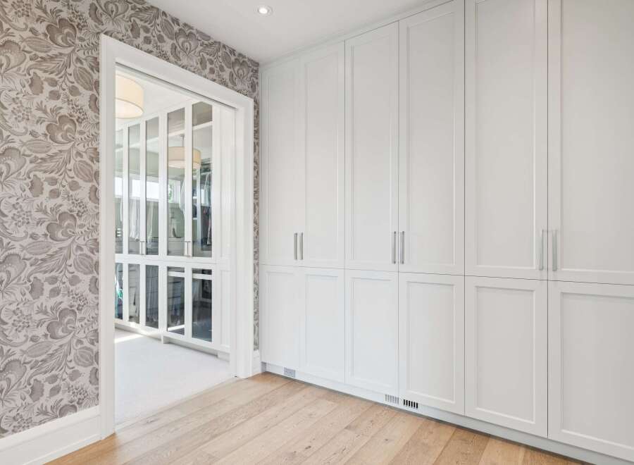 Discover this elegant walk-in closet featuring a sophisticated floral wallpaper and custom white cabinetry.