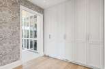 Discover this elegant walk-in closet featuring a sophisticated floral wallpaper and custom white cabinetry.