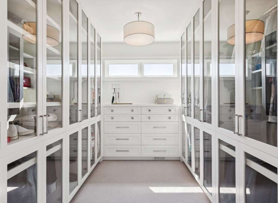 Step into this impeccably organized walk-in closet, featuring floor-to-ceiling glass-fronted cabinetry for a sophisticated display of your wardrobe.