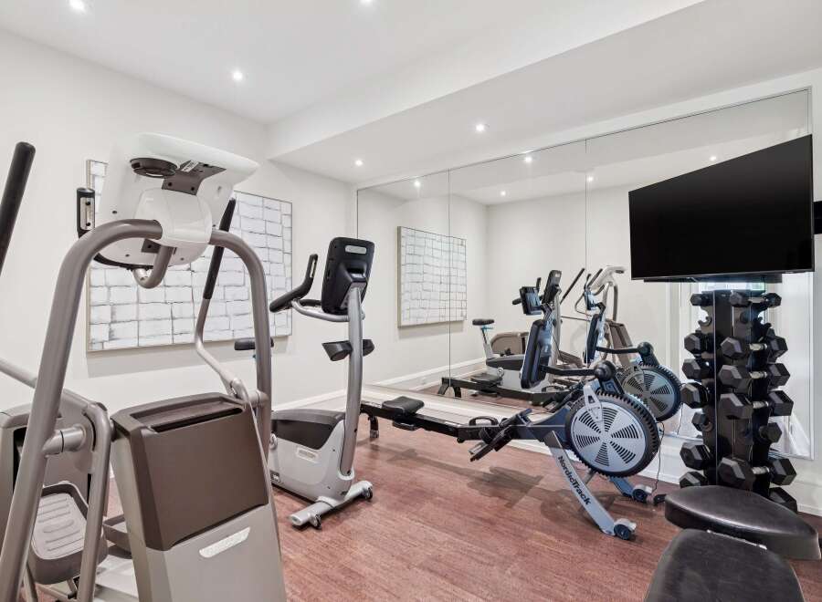 Elevate your fitness routine in this state-of-the-art home gym, featuring a Precor elliptical, a NordicTrack rower, and a comprehensive dumbbell rack.