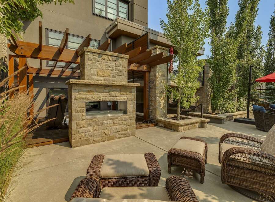 Experience luxurious outdoor living with this stunning patio featuring a modern stone fireplace and a beautiful wooden pergola.