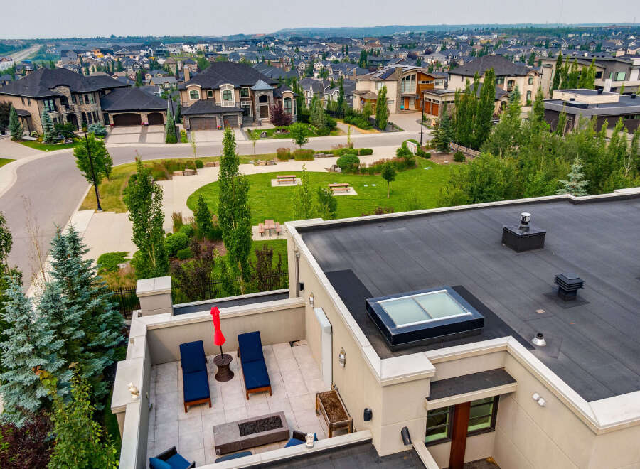Experience luxury living in this stunning property featuring a spacious rooftop patio with lounge chairs, a fire pit, and a vibrant red umbrella, perfect for outdoor entertaining.