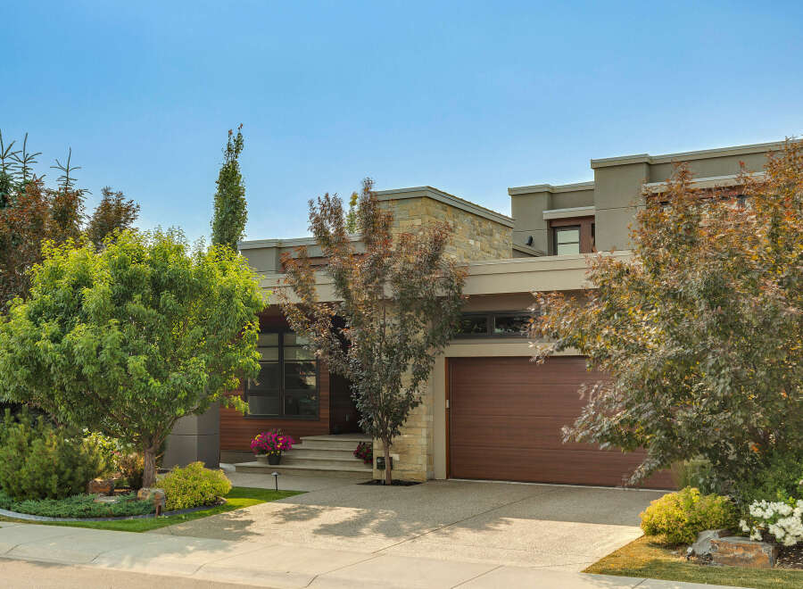 Discover this stunning modern home featuring a striking stone and stucco exterior, complemented by a warm wood garage door.