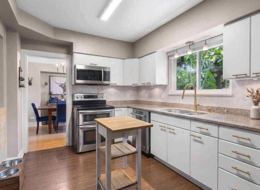 This modern kitchen features sleek white cabinetry with elegant gold hardware, complemented by a granite countertop and a stylish herringbone tile backsplash.