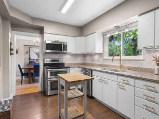 This modern kitchen features sleek white cabinetry with elegant gold hardware, complemented by a granite countertop and a stylish herringbone tile backsplash.
