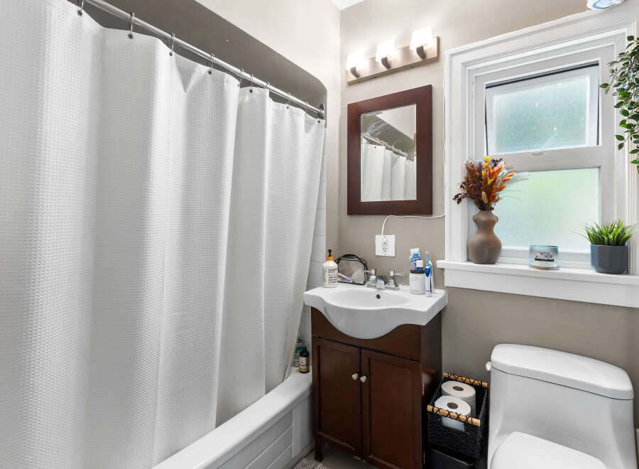 This charming bathroom features a pristine white bathtub with a textured shower curtain, complemented by a sleek vanity with a modern sink and ample storage.