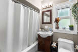 This charming bathroom features a pristine white bathtub with a textured shower curtain, complemented by a sleek vanity with a modern sink and ample storage.