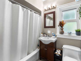 This charming bathroom features a pristine white bathtub with a textured shower curtain, complemented by a sleek vanity with a modern sink and ample storage.
