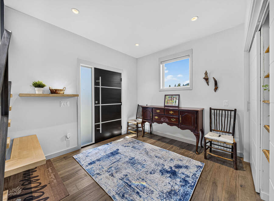 Step into this inviting entryway featuring a modern black door with sleek silver accents, complemented by a stylish area rug and a charming antique sideboard.