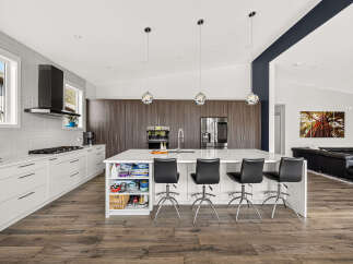 Experience modern luxury in this stunning kitchen, featuring sleek white cabinetry, a spacious island with waterfall countertops, and a sophisticated dark wood backsplash.