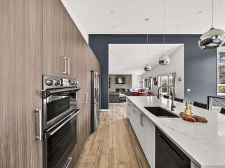 Experience modern luxury in this stunning kitchen, featuring sleek, wood-grain cabinetry and a spacious island with a waterfall countertop.