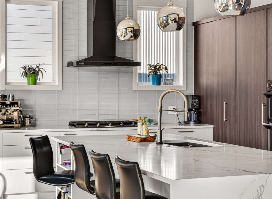 Experience modern luxury in this stunning kitchen, featuring sleek white cabinetry, a sophisticated dark range hood, and a beautiful marble island perfect for entertaining.