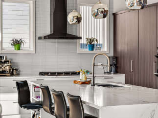 Experience modern luxury in this stunning kitchen, featuring sleek white cabinetry, a sophisticated dark range hood, and a beautiful marble island perfect for entertaining.