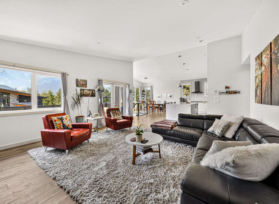 Experience modern living in this spacious open-concept home, featuring a sleek black leather sectional sofa and comfortable red accent chairs.