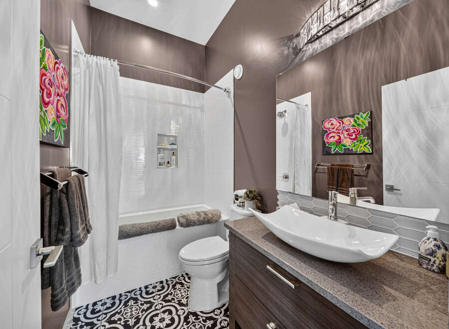 This modern bathroom features a sleek vessel sink atop a dark wood vanity, complemented by a striking floral art piece.