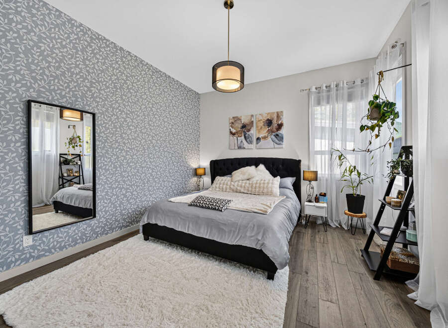 This bedroom features a stylish grey leaf-patterned accent wall, complemented by a plush white rug and a dark upholstered bed.