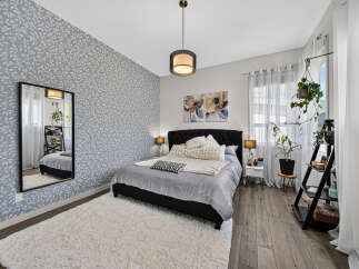 This bedroom features a stylish grey leaf-patterned accent wall, complemented by a plush white rug and a dark upholstered bed.