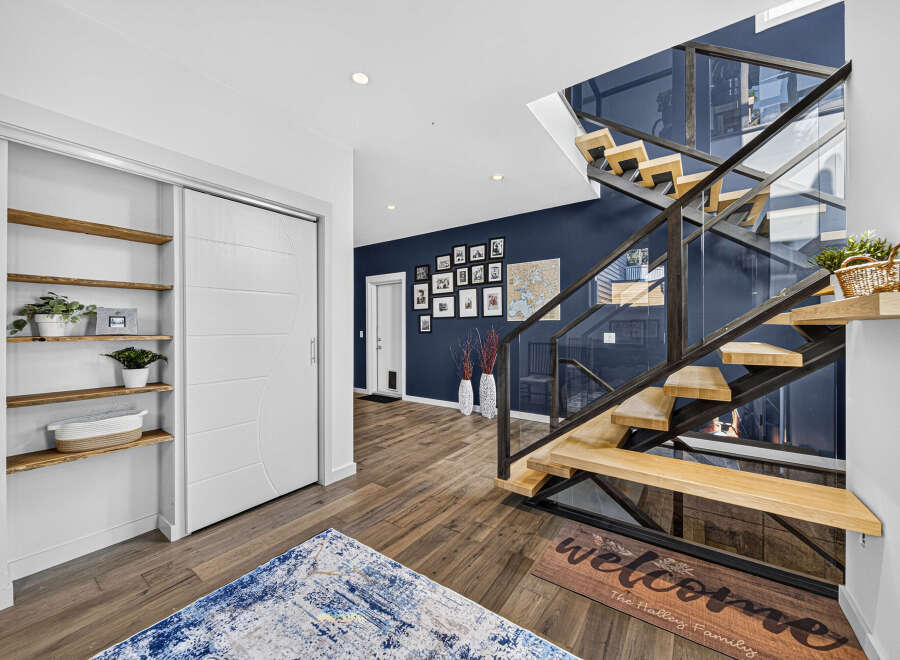 Step into a modern entryway featuring a striking floating staircase with glass railings and warm wood treads.