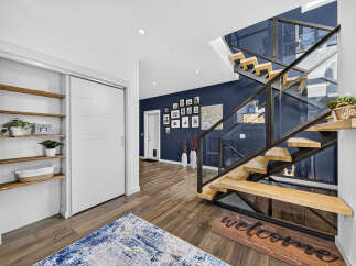 Step into a modern entryway featuring a striking floating staircase with glass railings and warm wood treads.