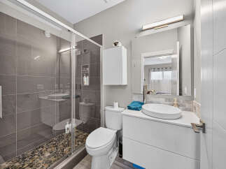 Experience modern luxury in this stunning bathroom, featuring a sleek glass-enclosed shower with elegant grey tile and a unique pebble floor.