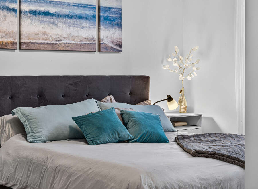 Experience coastal serenity in this inviting bedroom, featuring a plush tufted headboard and a triptych artwork depicting serene ocean waves.