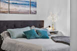 Experience coastal serenity in this inviting bedroom, featuring a plush tufted headboard and a triptych artwork depicting serene ocean waves.