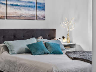 Experience coastal serenity in this inviting bedroom, featuring a plush tufted headboard and a triptych artwork depicting serene ocean waves.