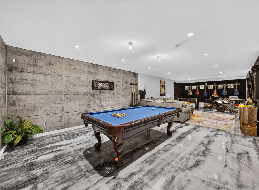 Experience ultimate entertainment in this modern basement featuring a professional pool table and a dedicated music area with guitars and a drum set.