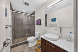 This modern bathroom features a sleek walk-in shower with pebble flooring and grey tiled walls, complemented by a contemporary white toilet and a stylish vessel sink vanity.