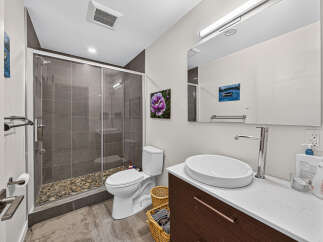 This modern bathroom features a sleek walk-in shower with pebble flooring and grey tiled walls, complemented by a contemporary white toilet and a stylish vessel sink vanity.