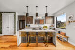 Experience modern living in this stunning kitchen featuring dark wood cabinetry, a sleek white island with bar seating, and contemporary pendant lighting.