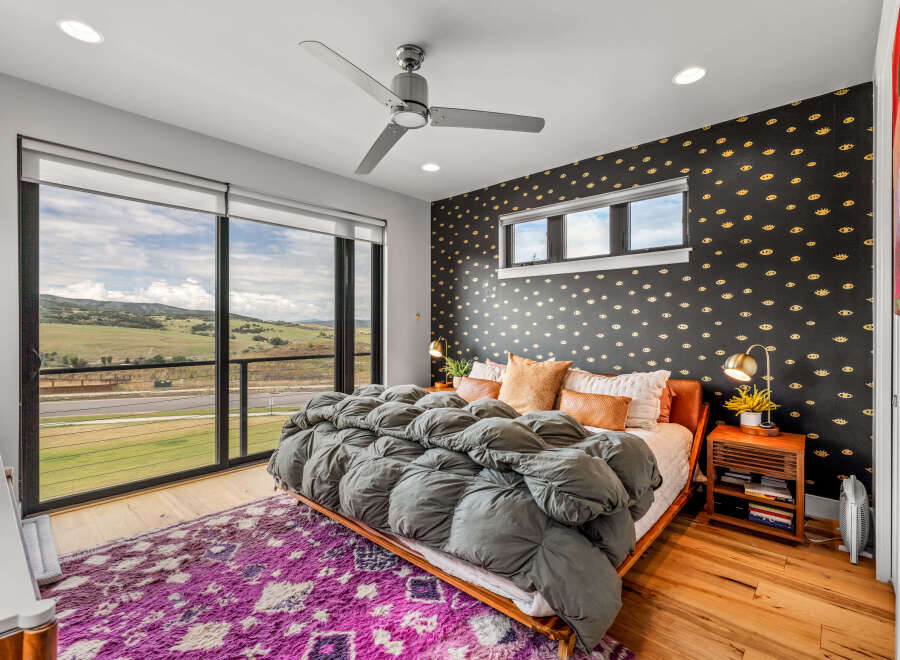 Experience luxury living in this stunning bedroom featuring a plush grey comforter on a wooden bed frame, complemented by a vibrant purple rug.