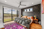 Experience luxury living in this stunning bedroom featuring a plush grey comforter on a wooden bed frame, complemented by a vibrant purple rug.