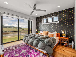 Experience luxury living in this stunning bedroom featuring a plush grey comforter on a wooden bed frame, complemented by a vibrant purple rug.