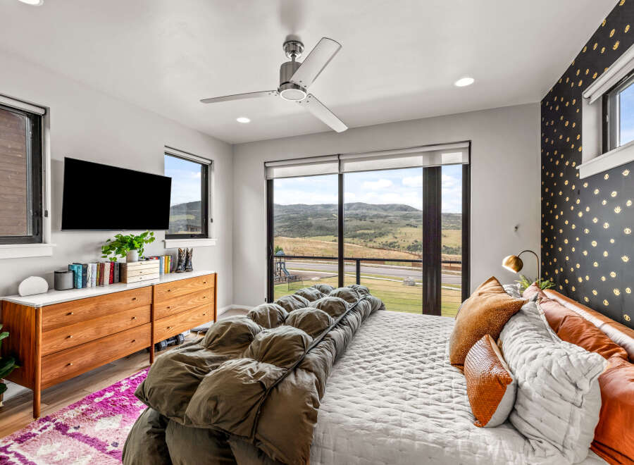 Experience modern luxury in this stunning bedroom featuring a sleek ceiling fan and a large flat-screen TV.