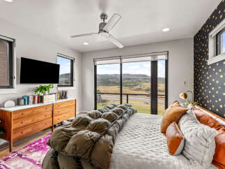 Experience modern luxury in this stunning bedroom featuring a sleek ceiling fan and a large flat-screen TV.