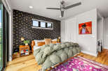 This stylish bedroom features a unique black wallpaper with a gold eye pattern, complemented by a plush green duvet and a vibrant purple rug.