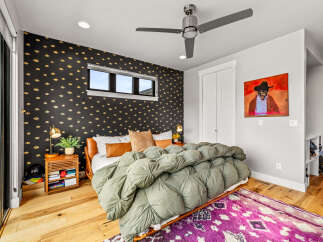 This stylish bedroom features a unique black wallpaper with a gold eye pattern, complemented by a plush green duvet and a vibrant purple rug.